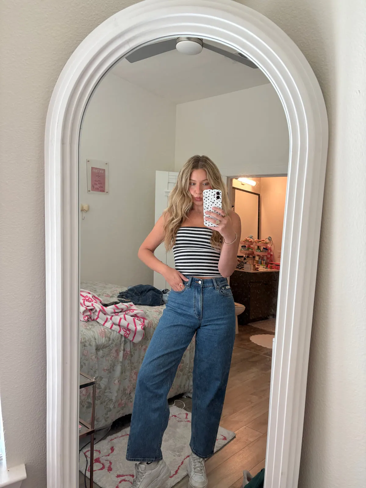 Macie in a black and white striped tank tucked into high-waisted straight-leg denim, reflected in a tall arched mirror.